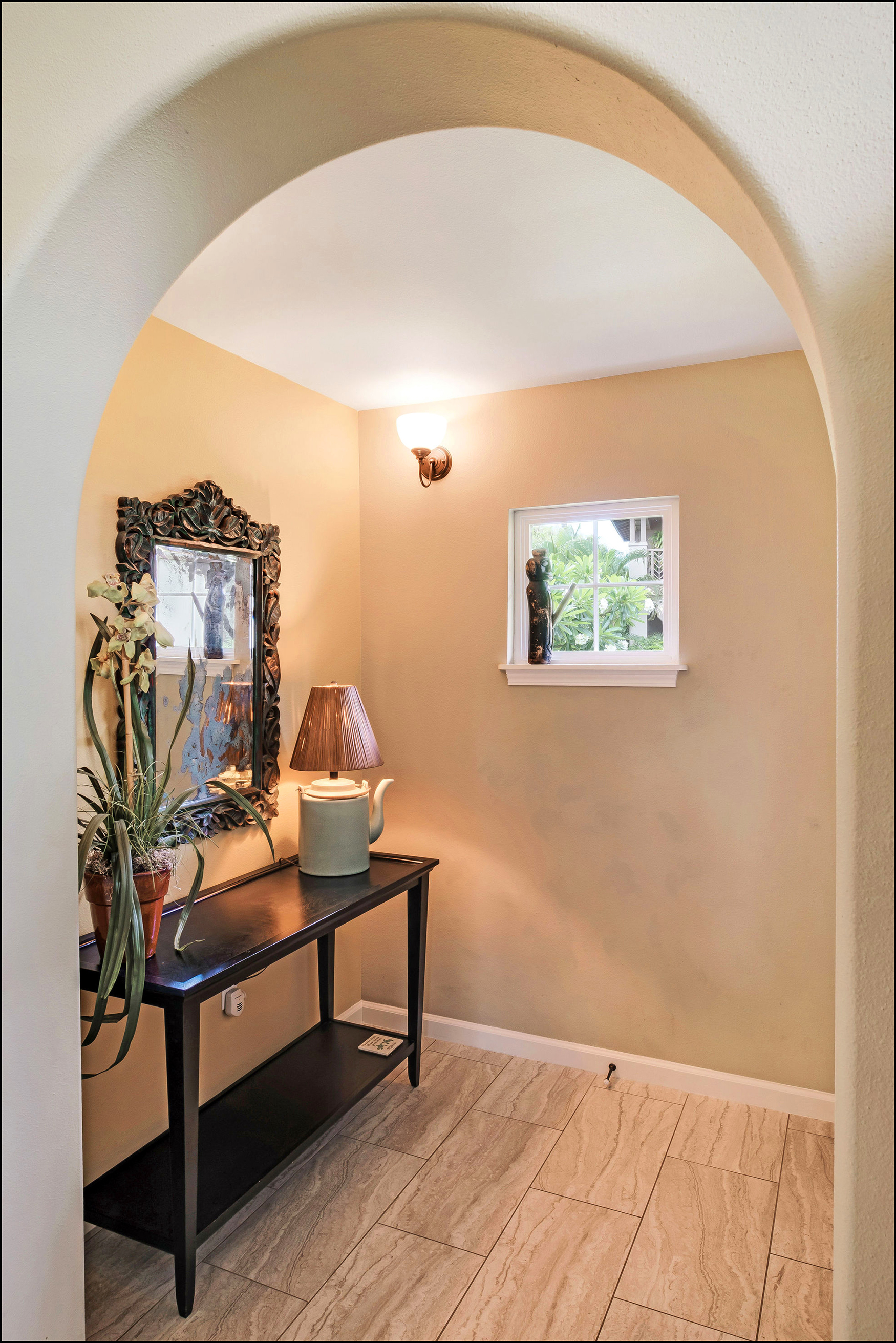 Tiled entry hall with carved wooden antique piece and carved wood mirror over a console